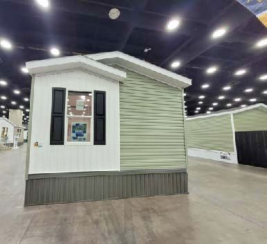 Small green and white mobile home display model inside an indoor showroom