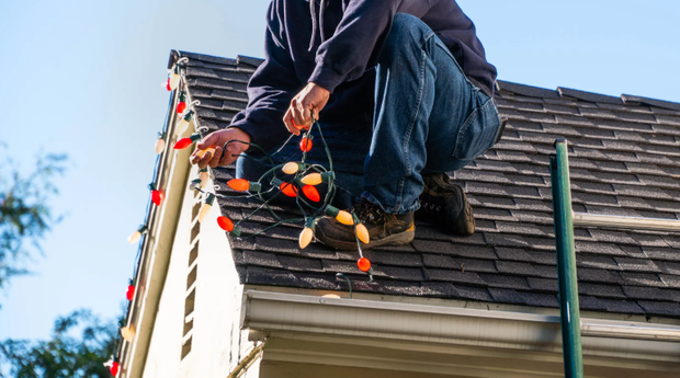 Person on a roof installing holiday lights on the house's edge.