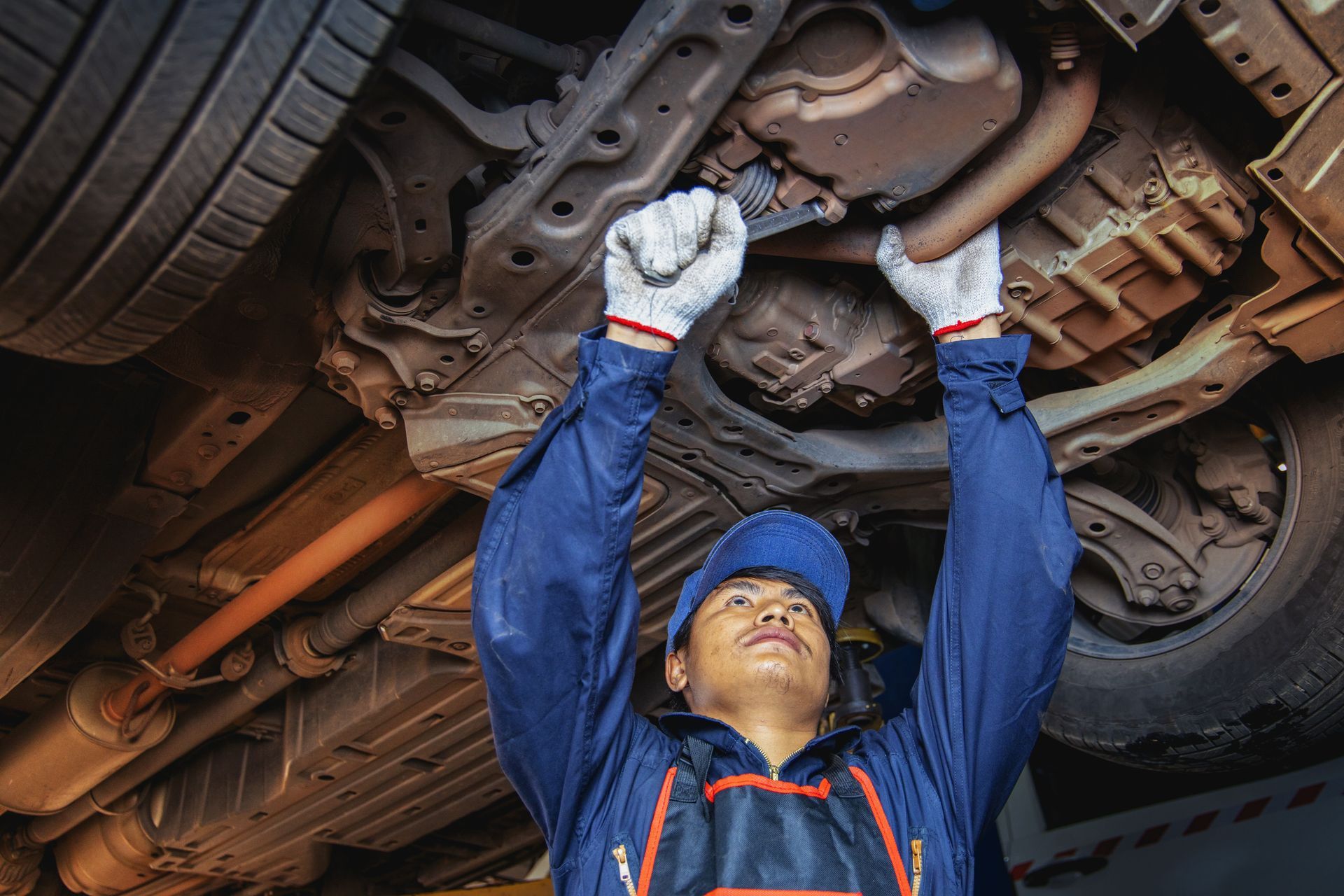Auto mechanic inspecting car brake rotor under lifted vehicle in repair garage.