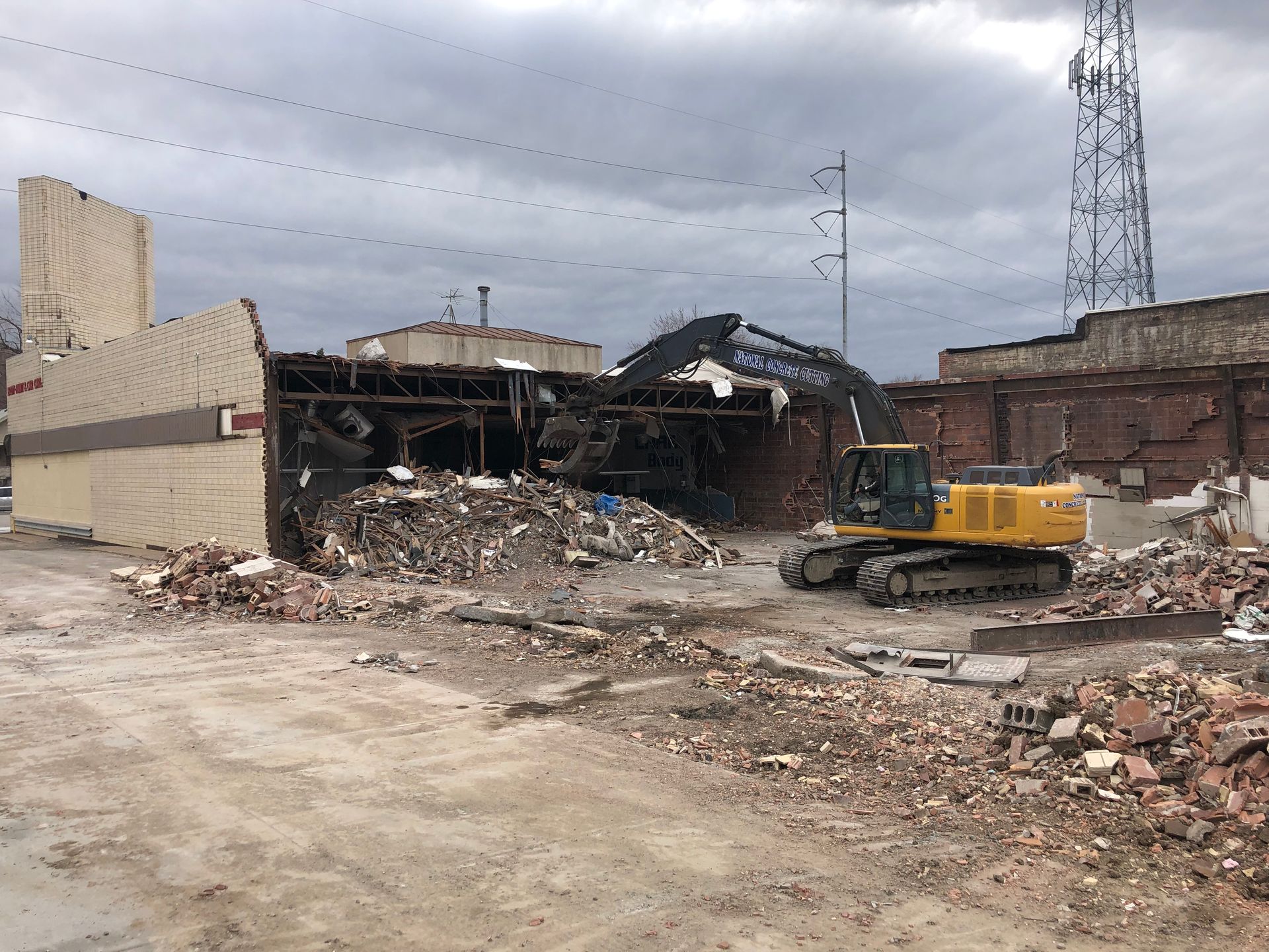 Demolition of a building site with an excavator amidst debris. Gray sky.