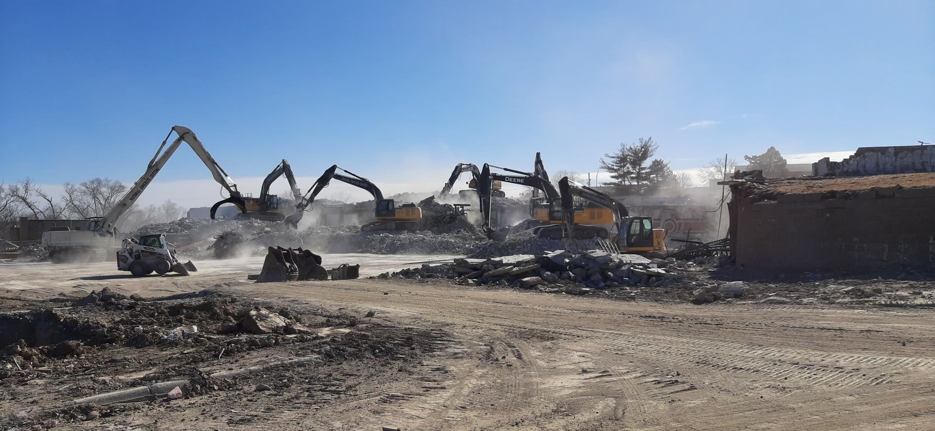 Demolition site with multiple excavators tearing down a building on a sunny day.