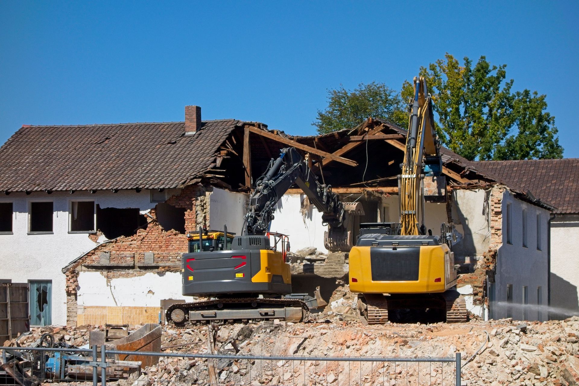 Demolition of old house by excavator with debris flying during building destruction process.