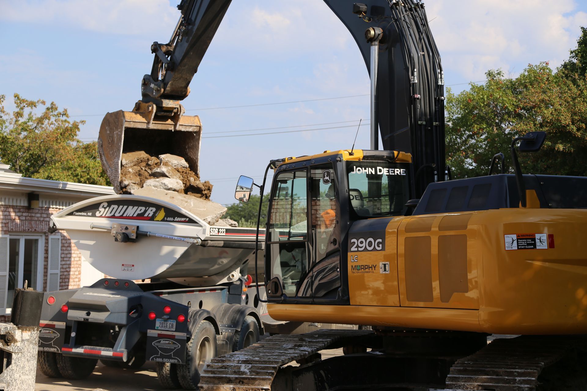 Excavator loading a dump trailer with debris at a construction site.