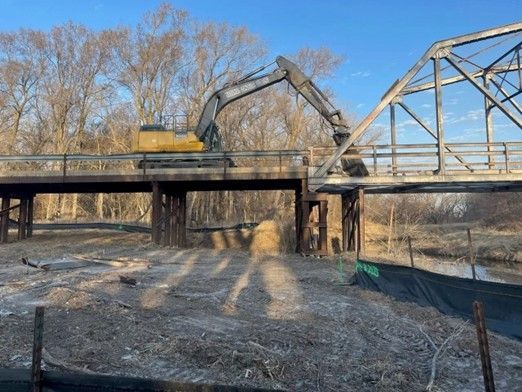 Excavator performing building demolition with debris and dust at active construction site.