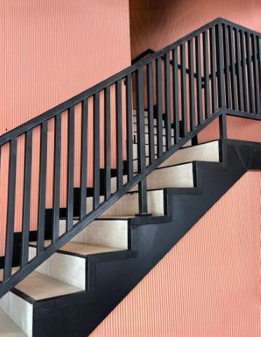 Black handrail staircase with peach-colored wall in a modern Suffolk home.