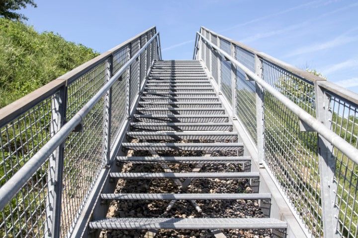 Staircase leading upwards, flanked by railings, under a blue sky, and a grassy hill.