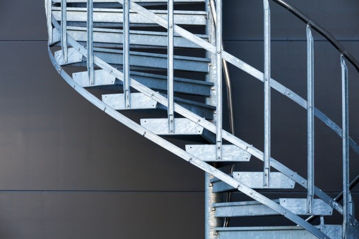 Metal spiral staircase against a gray wall.