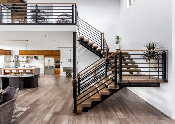 Modern two-story interior with a wooden staircase and balcony. Black railings, white walls, and wood flooring.