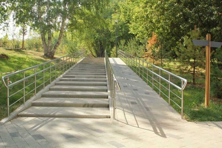 Staircase and ramp in a park, with trees in the background and a sign.