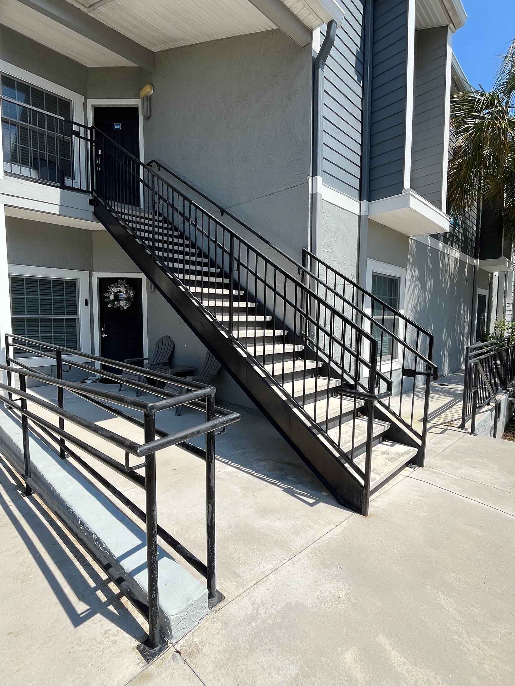 Staircase leading upwards, flanked by railings, under a blue sky, and a grassy hill.