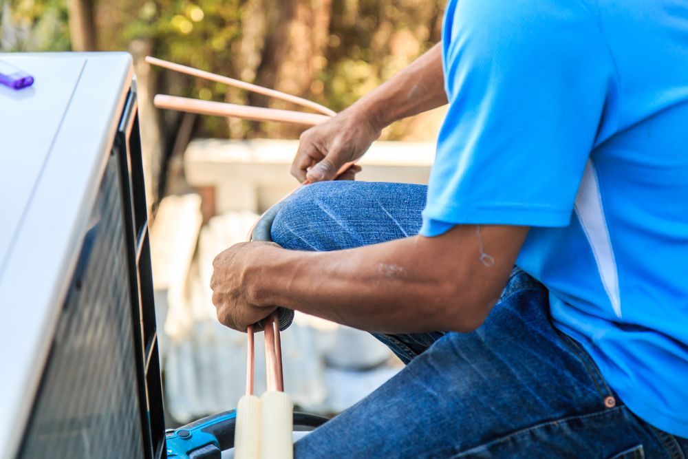 A Man in a Blue Shirt is Working on an Air Conditioner — Davies Refrigeration & Air Conditioning in Warana, QLD