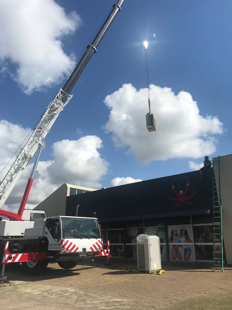 A Large Crane is Lifting a Box in the Air in Front of a Building — Davies Refrigeration & Air Conditioning in Warana, QLD