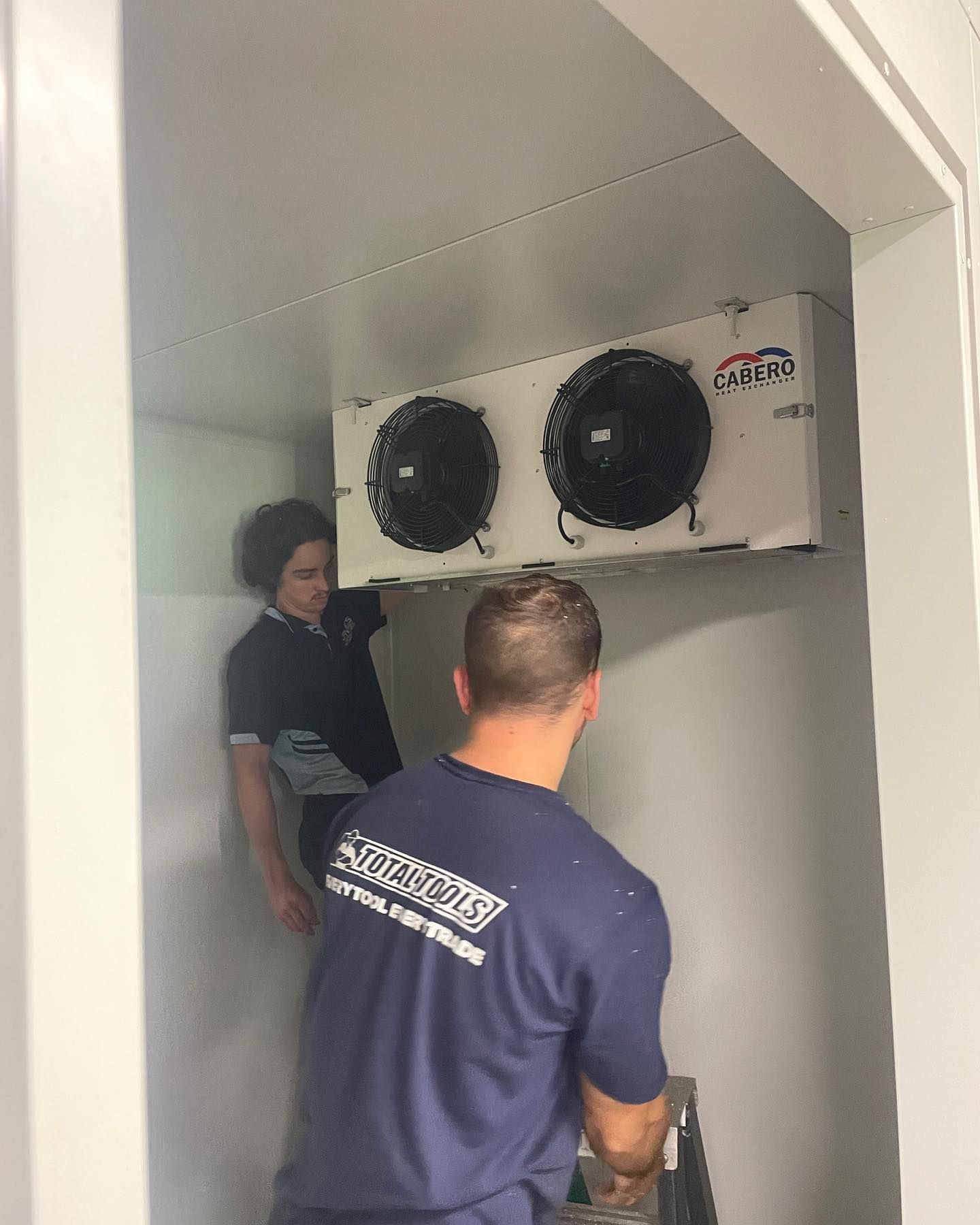 A Man in a Blue Shirt is Working on a Refrigerator — Davies Refrigeration & Air Conditioning in Warana, QLD