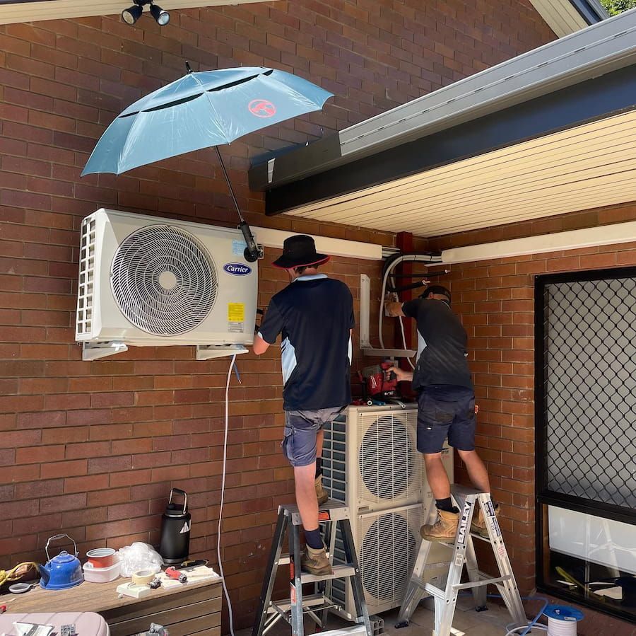 Two Men Are Working on an Air Conditioner on a Brick Wall — Davies Refrigeration & Air Conditioning in Warana, QLD