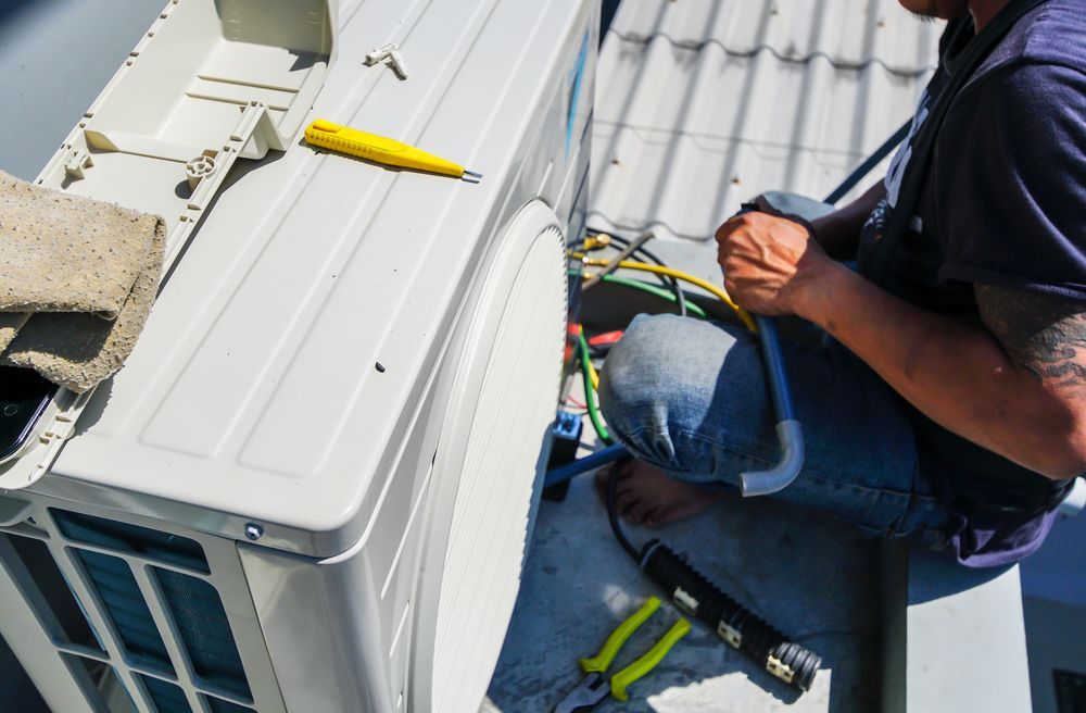 A Man is Sitting on a Roof Fixing an Air Conditioner — Davies Refrigeration & Air Conditioning in Cooroy, QLD