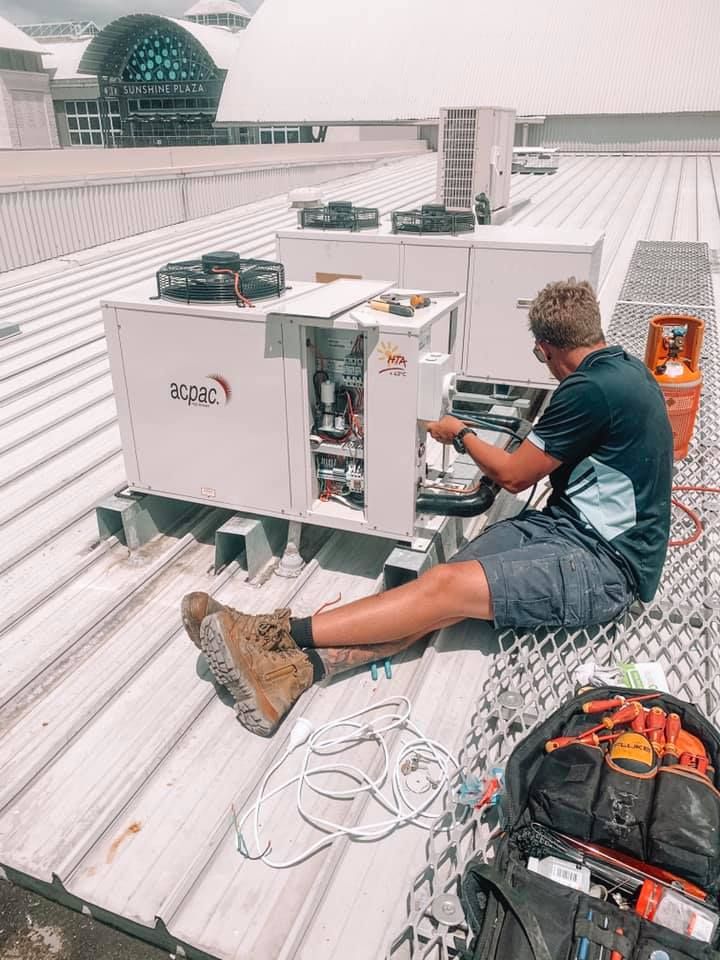 A Man is Sitting on a Roof Working on a Machine — Davies Refrigeration & Air Conditioning in Warana, QLD