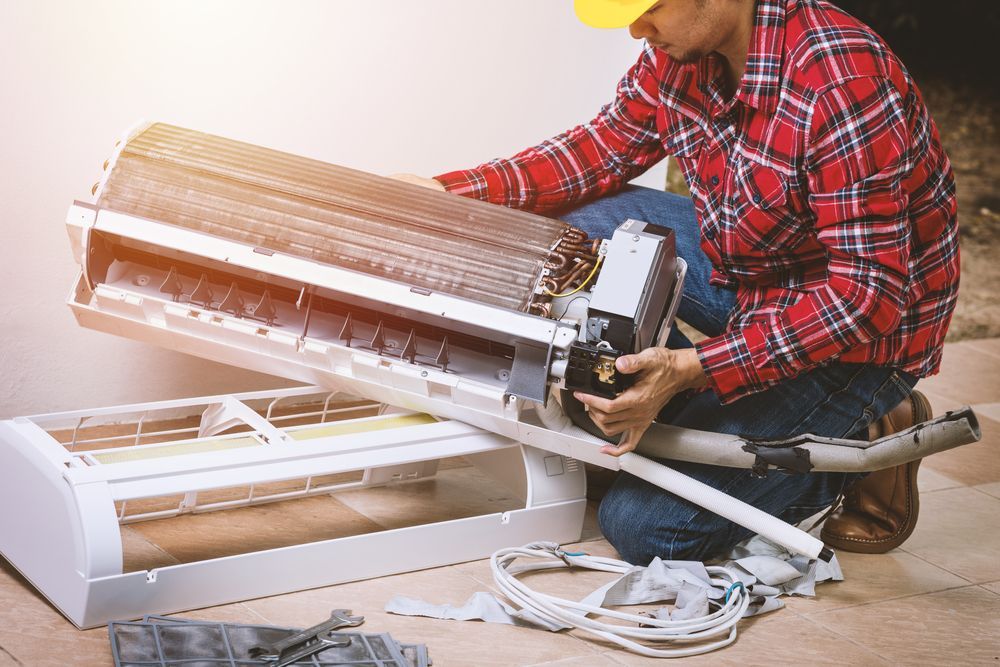 A Man is Repairing an Air Conditioner on the Floor — Davies Refrigeration & Air Conditioning in Noosa, QLD