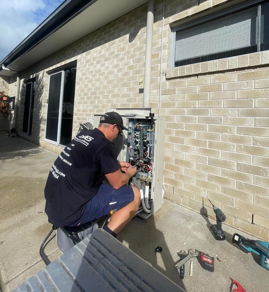 A Man is Working on a Machine Outside of a Brick Building — Davies Refrigeration & Air Conditioning in Warana, QLD
