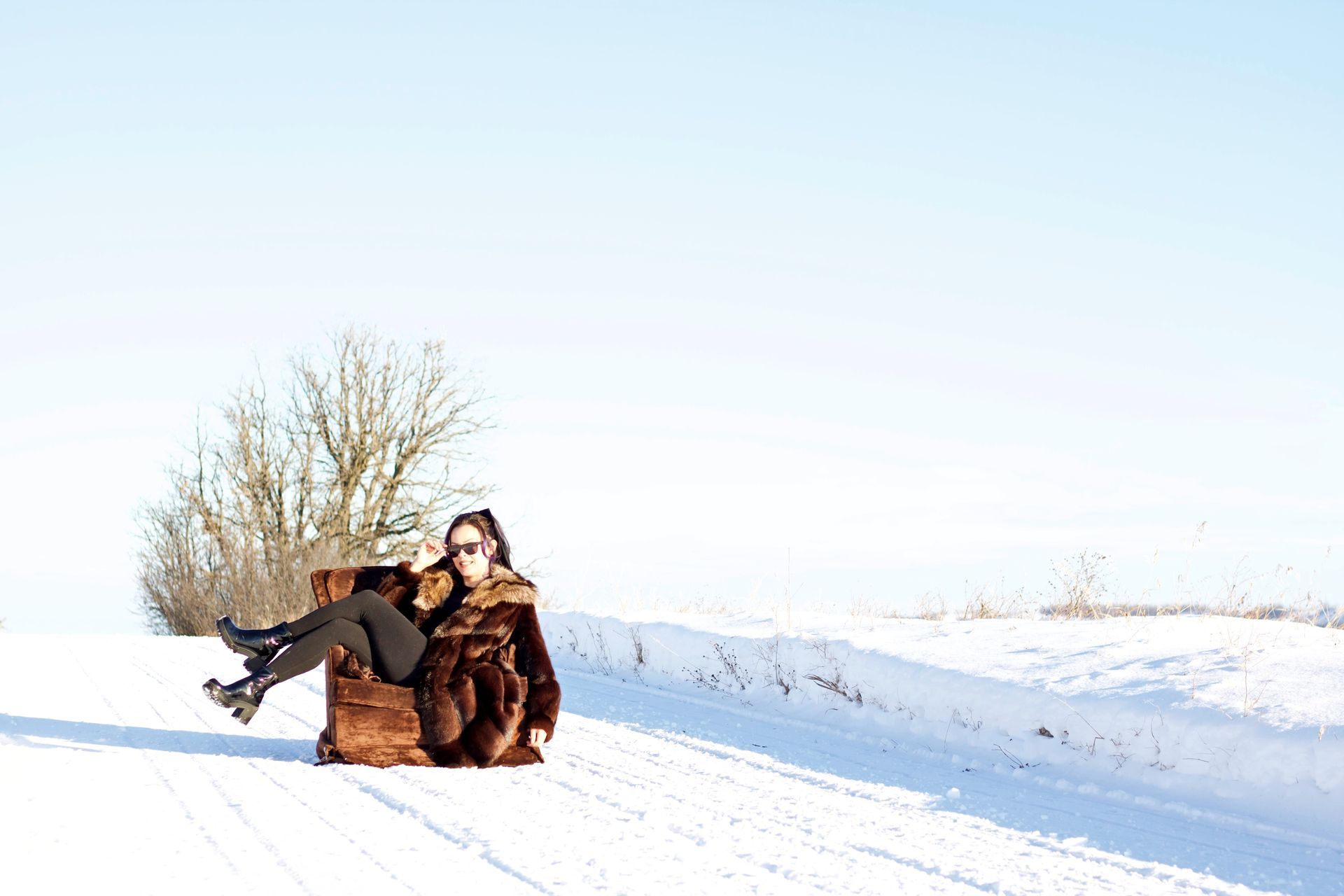Woman in fur coat sits on an armchair in a snowy landscape.