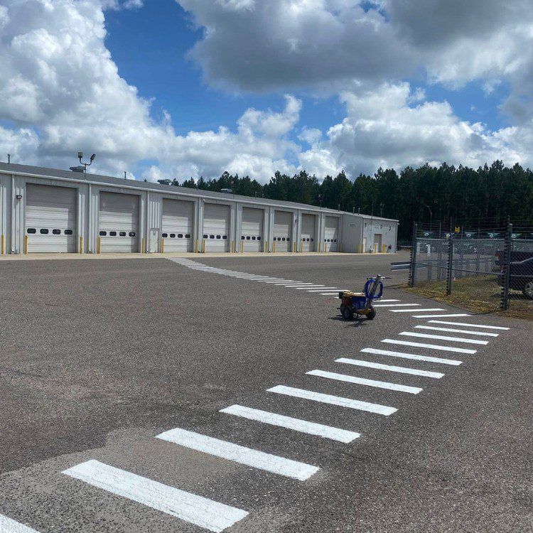 Exterior view of a building with several garage doors, crosswalk in foreground. Painting machine in the crosswalk, blue sky.