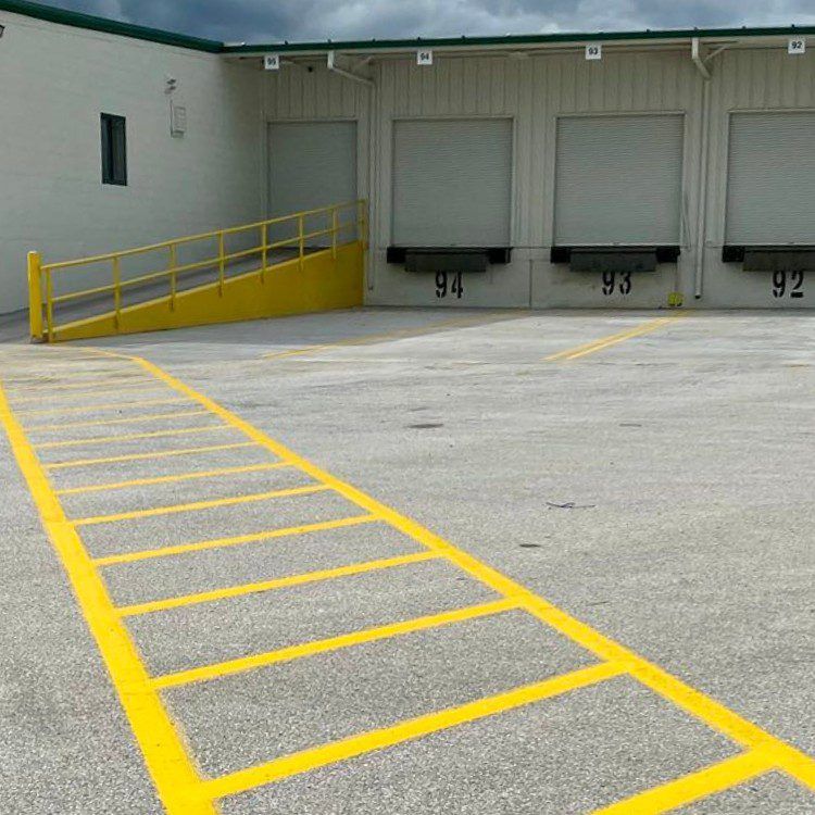 Exterior of a loading dock with yellow painted lines. Ramps, dock doors 92-94 are visible.