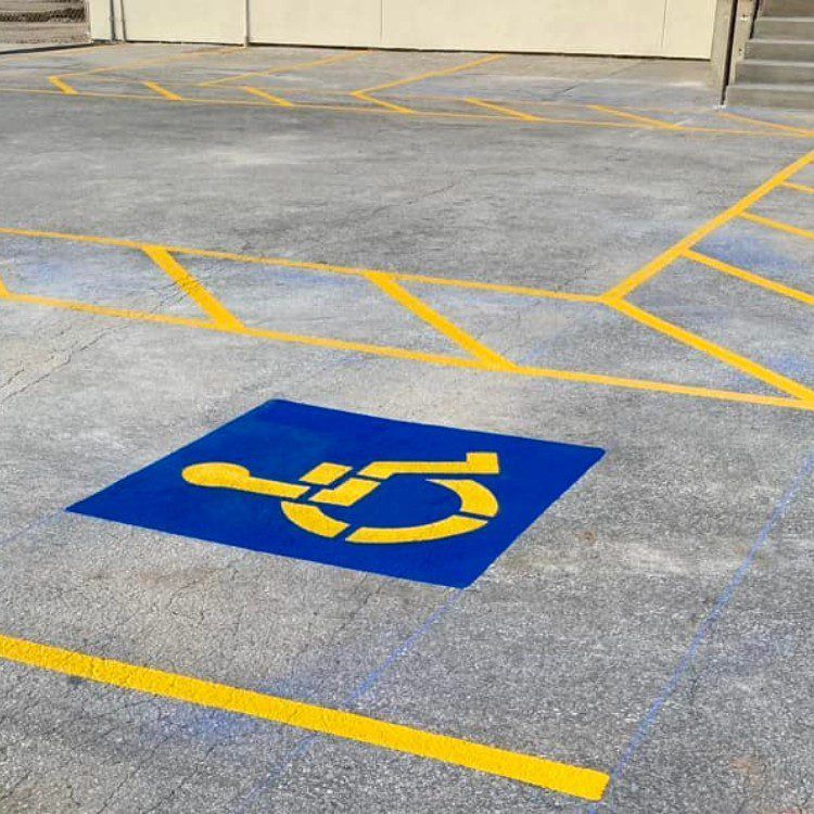 Blue and yellow handicap parking space in a concrete lot with yellow parking lines.