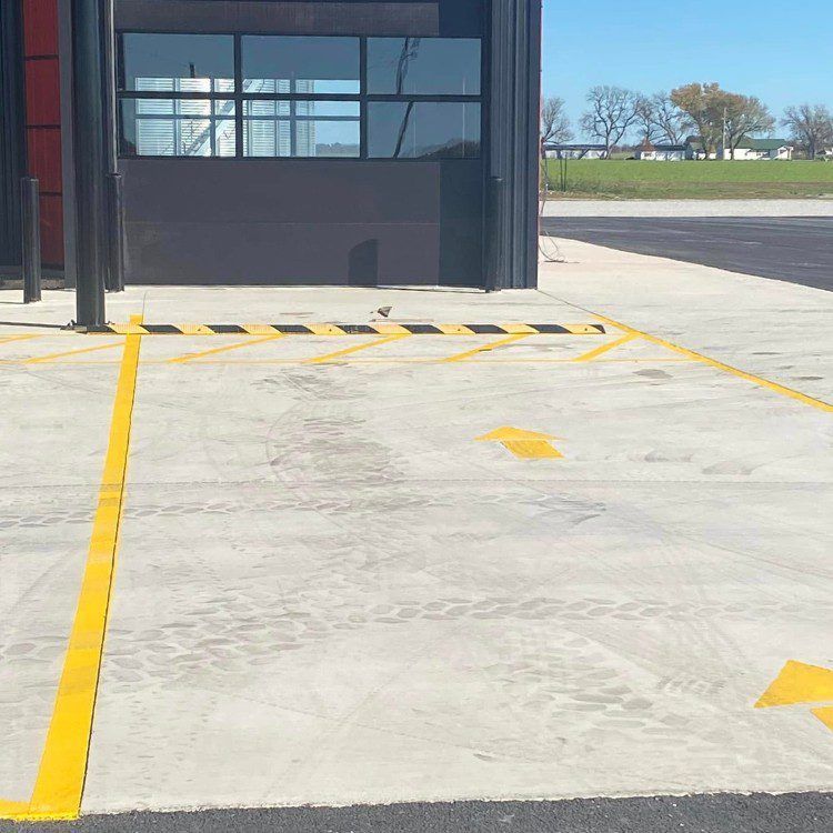 Concrete parking space marked with yellow lines and arrows, next to a building.