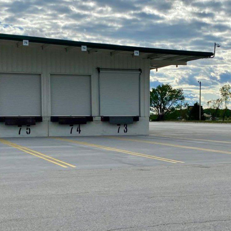 Loading docks 73, 74, and 75 on a warehouse. The concrete apron has yellow lines. Cloudy sky.
