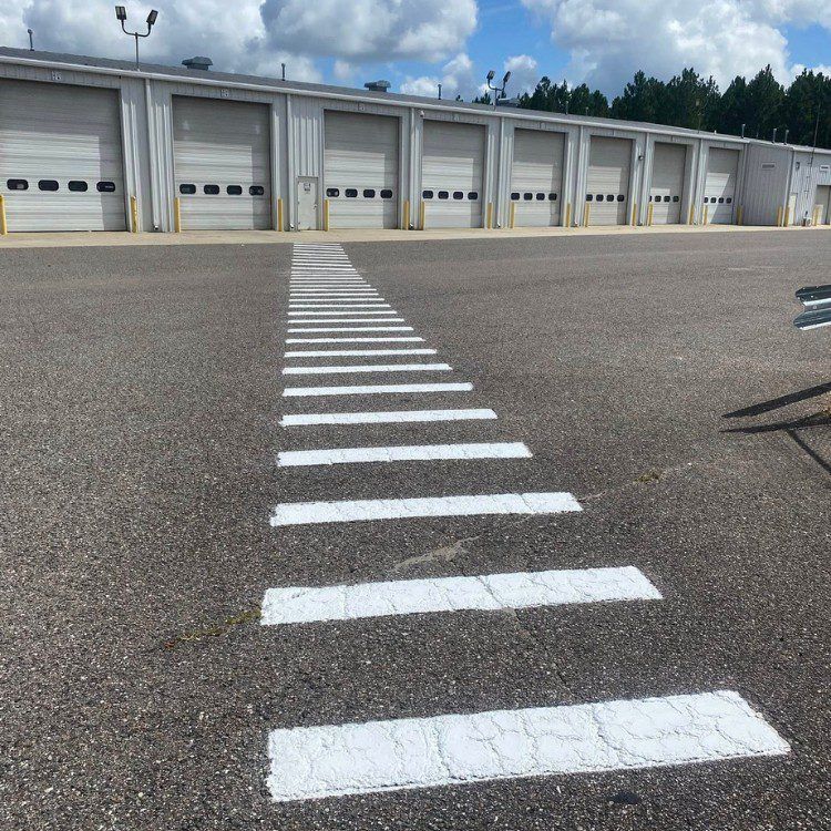 Striped crosswalk in front of a row of warehouse garage doors under a cloudy sky.