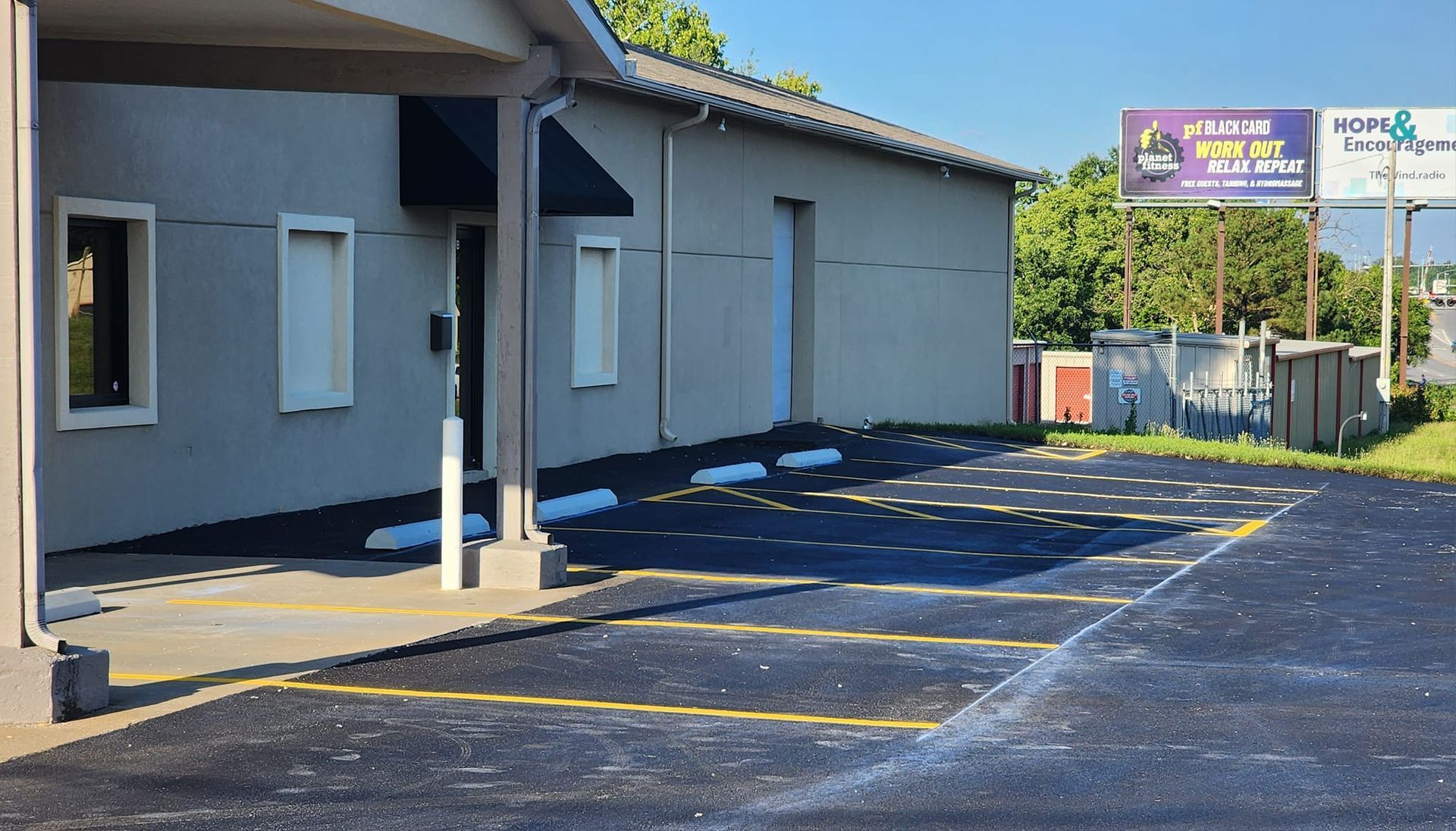 Exterior of a gray building with parking spaces. Sign for storage and businesses visible in the background.