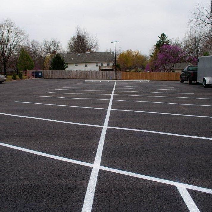 Empty asphalt parking lot with white lines, overcast sky, and suburban homes in background.