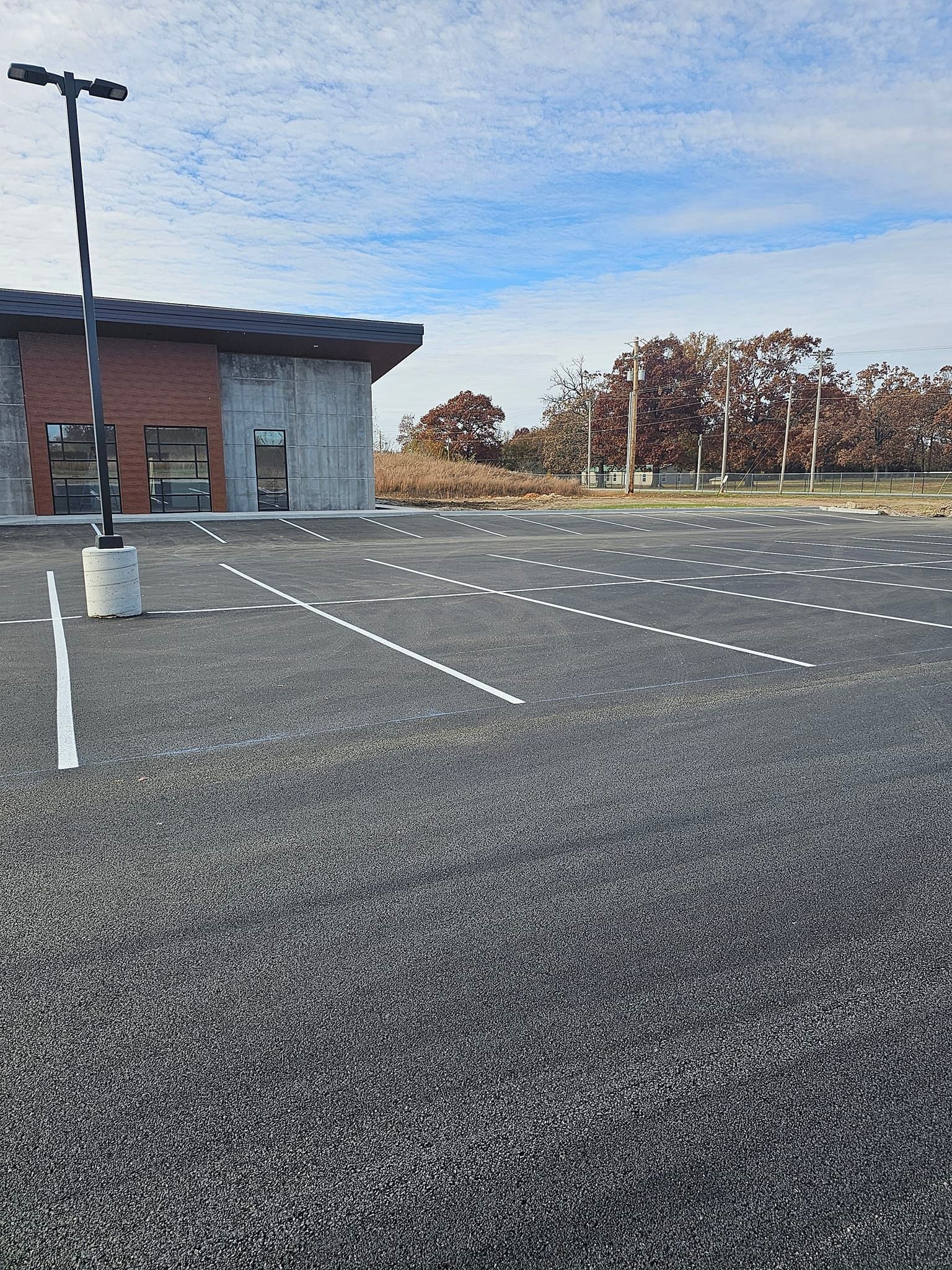 Empty asphalt parking lot with white painted lines, a building, and a cloudy sky.