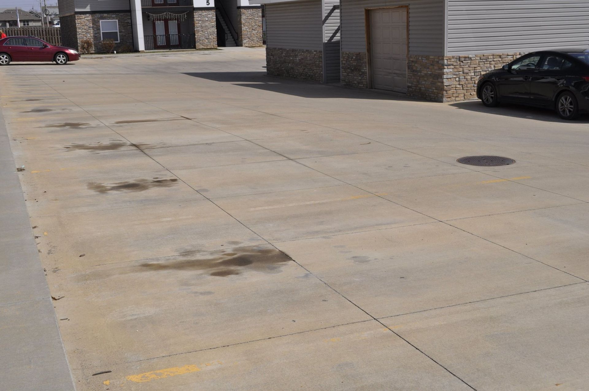 Concrete parking lot with parked cars and building in background.