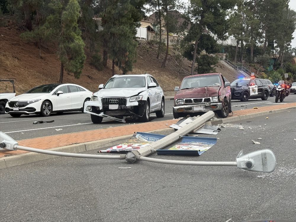Car accident scene with damaged cars, fallen utility pole, and police lights on a street.