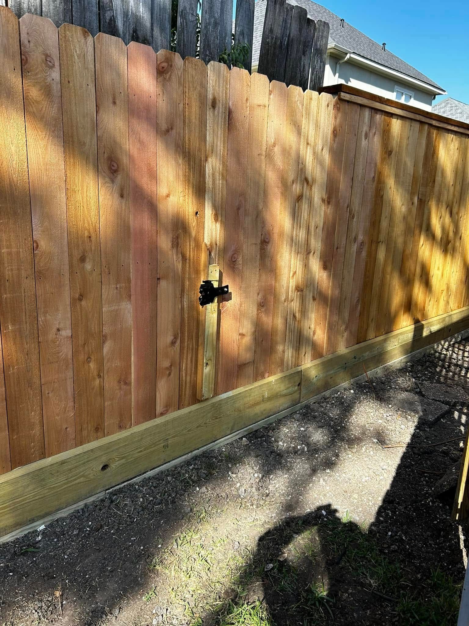 Wooden fence with latch, casting a long shadow on a sunny day.