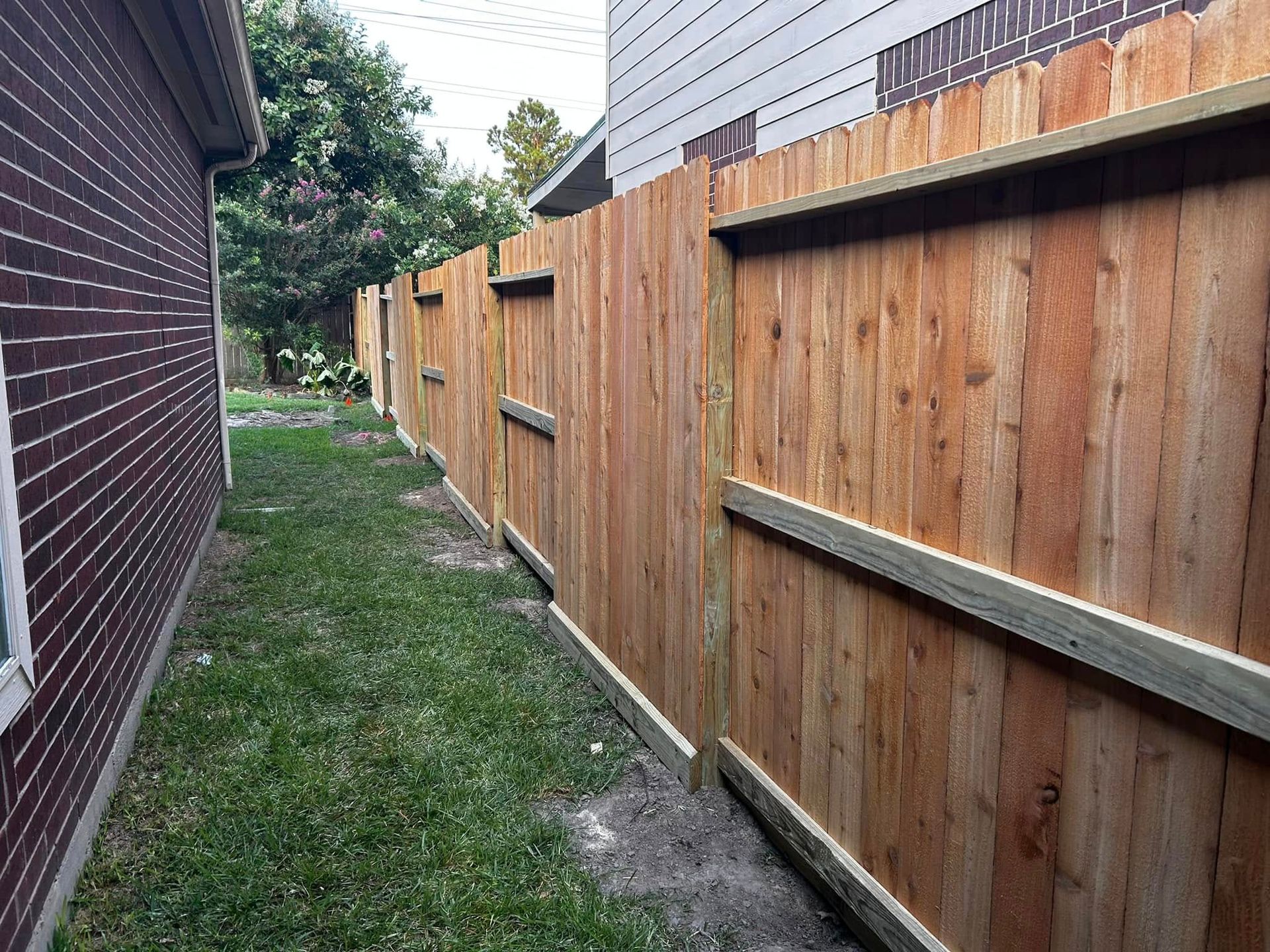 Wooden fence along a grassy side yard between two buildings.