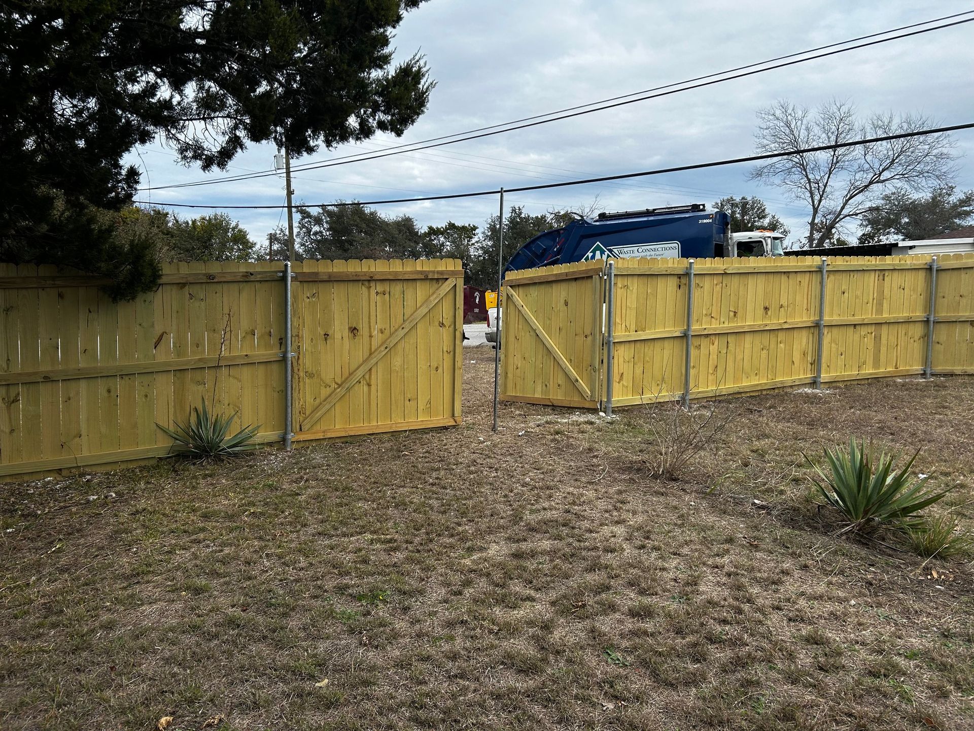 Wooden fence with open gate in a grassy yard, with a blue vehicle visible in the background.