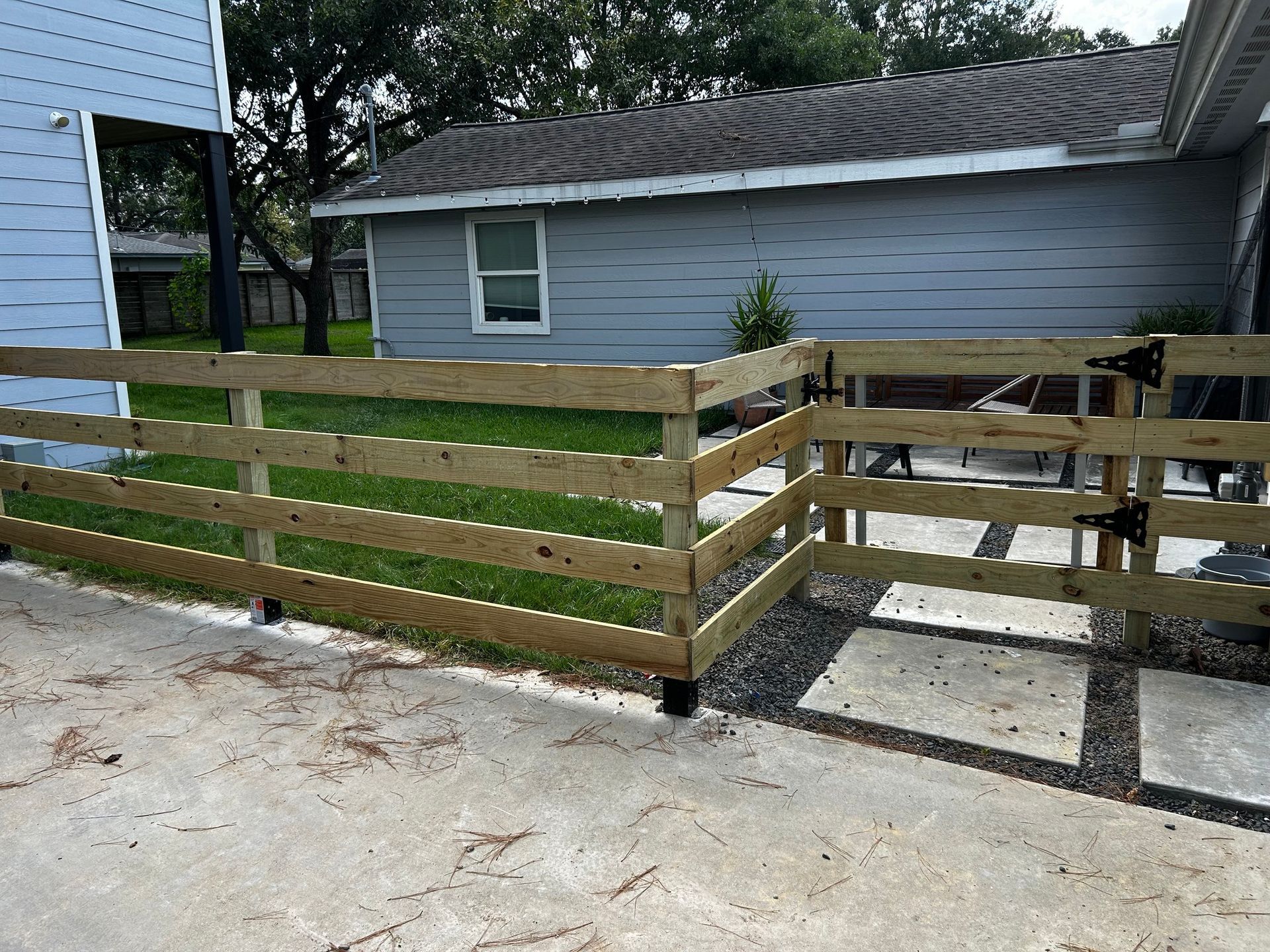 Wooden fence with gate, enclosing a grassy area next to a light blue house.