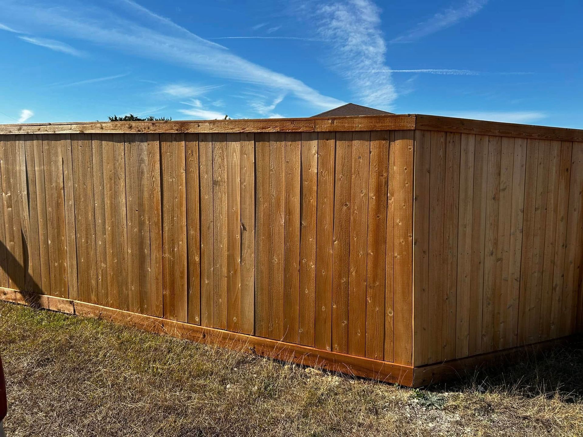 Wooden fence in a corner setting against a bright blue sky with wispy clouds.