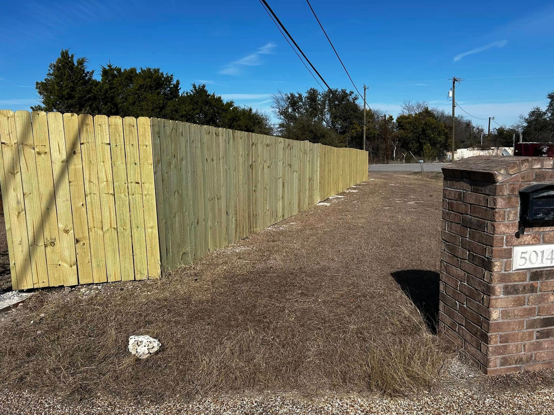 Wooden fence with a brick mailbox in front, roadside setting.