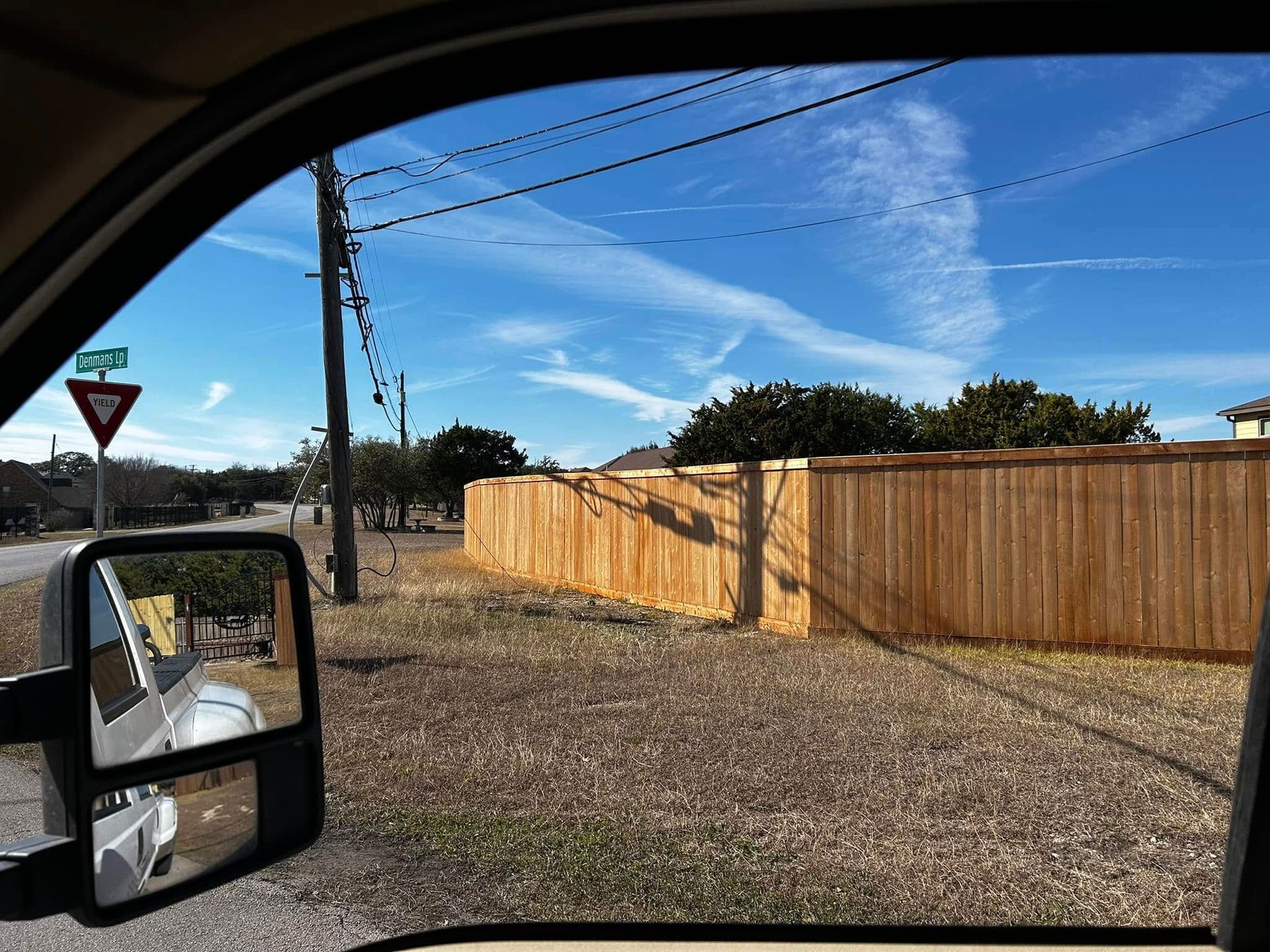 View from a vehicle of a street with a wooden fence under a bright blue sky.