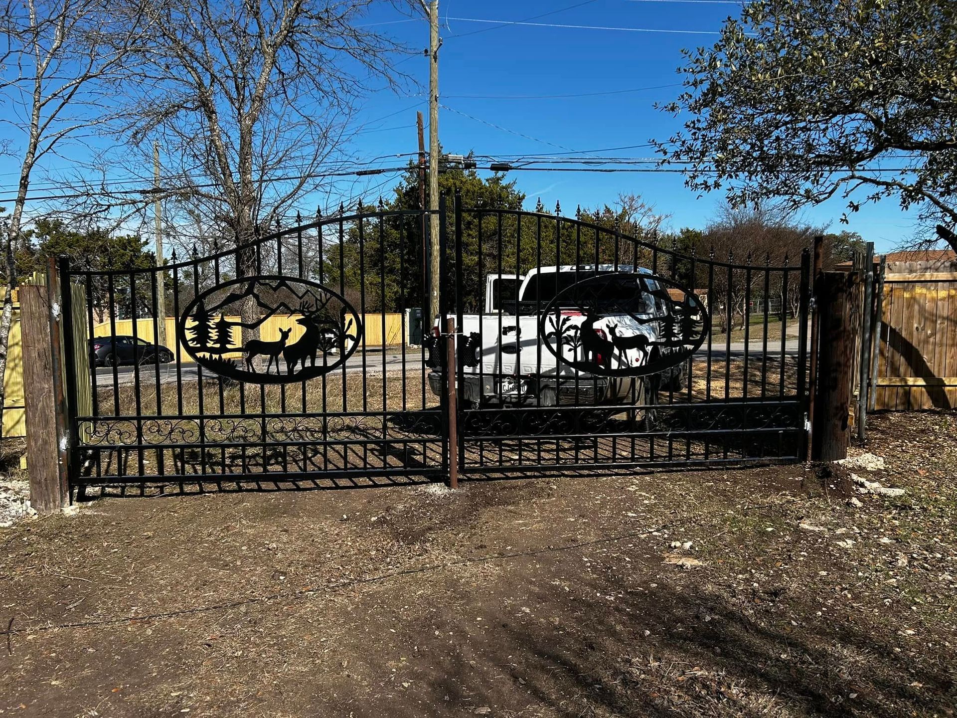 Black metal gate with a ranch scene design, fronting a driveway. A white pickup truck is parked behind it.