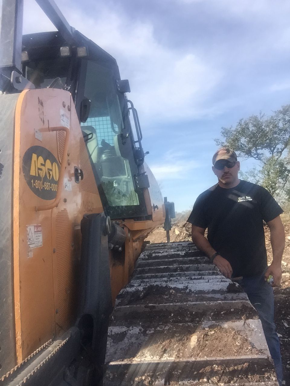 Man stands next to a bulldozer, with a blue sky background.