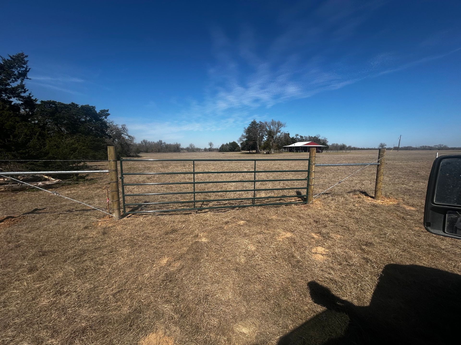 Metal gate in a field, with a house in the distance under a blue sky.