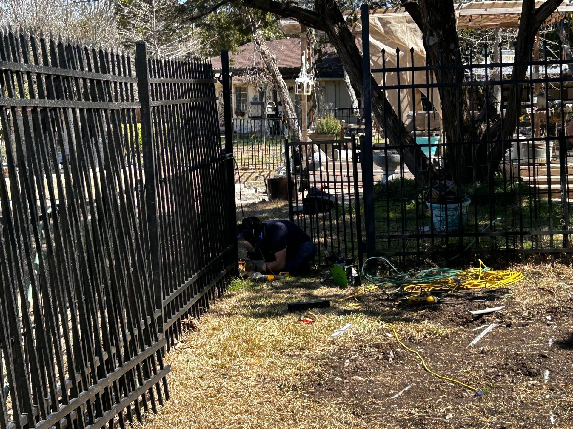 Person installing a black metal fence in a yard with sparse grass.