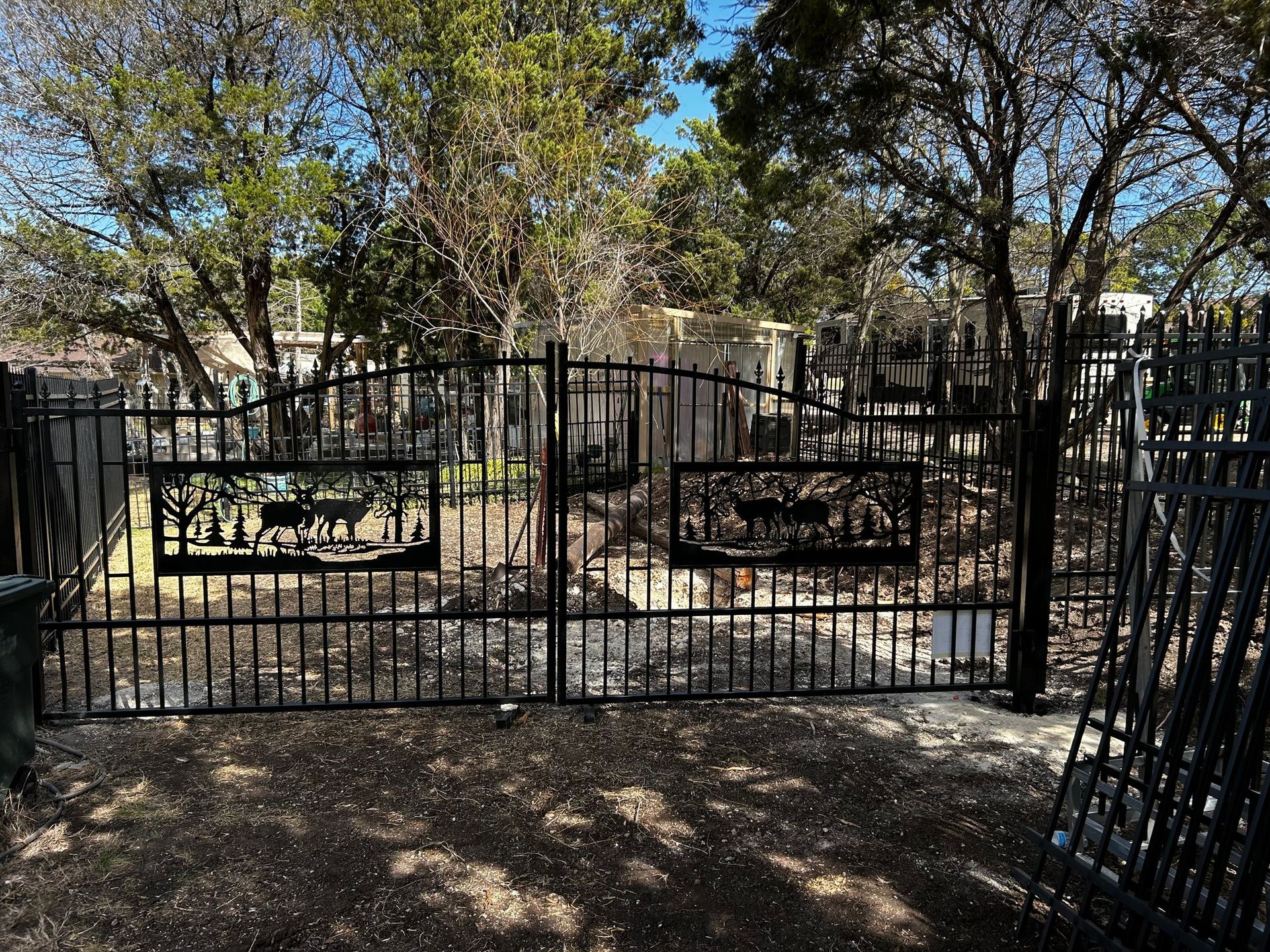 Black metal driveway gate with deer cutouts, set against trees.