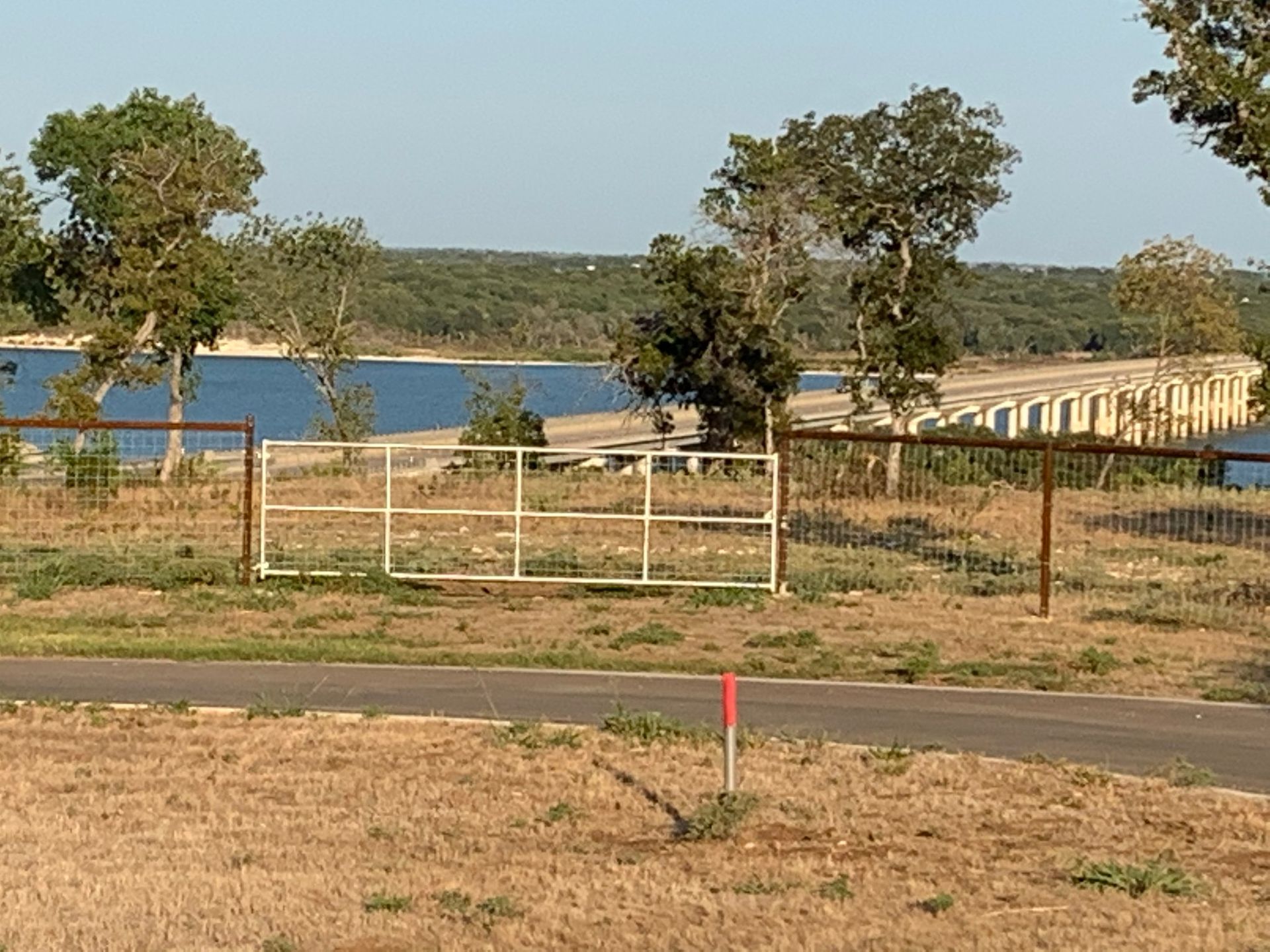 Gate open to a bridge over a lake, with trees and a light blue sky.