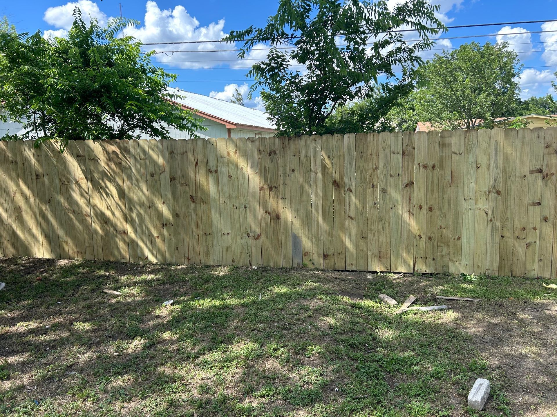 Wooden privacy fence in a grassy yard under a blue sky with clouds.