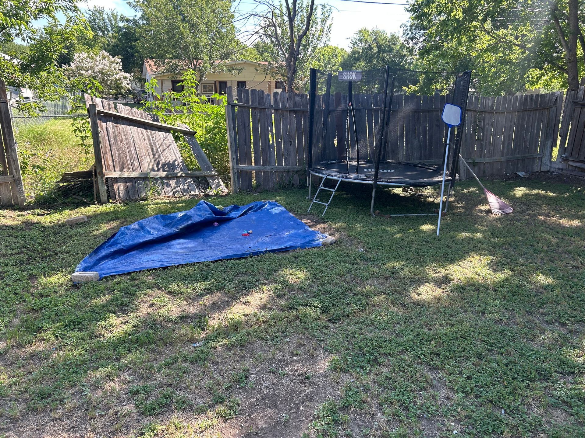 Backyard scene with a blue tarp, trampoline, and weathered wooden fence.