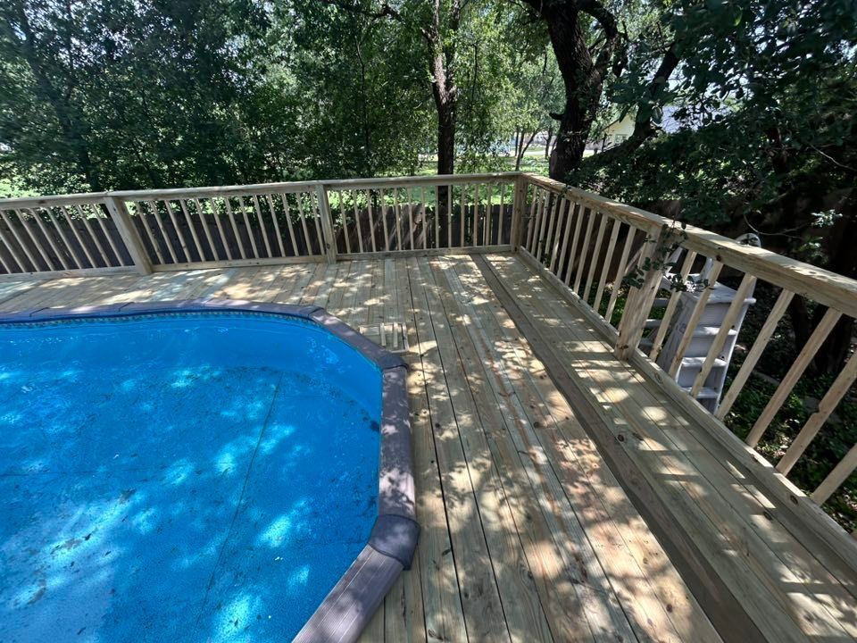 Wooden deck surrounding a blue swimming pool with a wooden railing in a backyard setting.